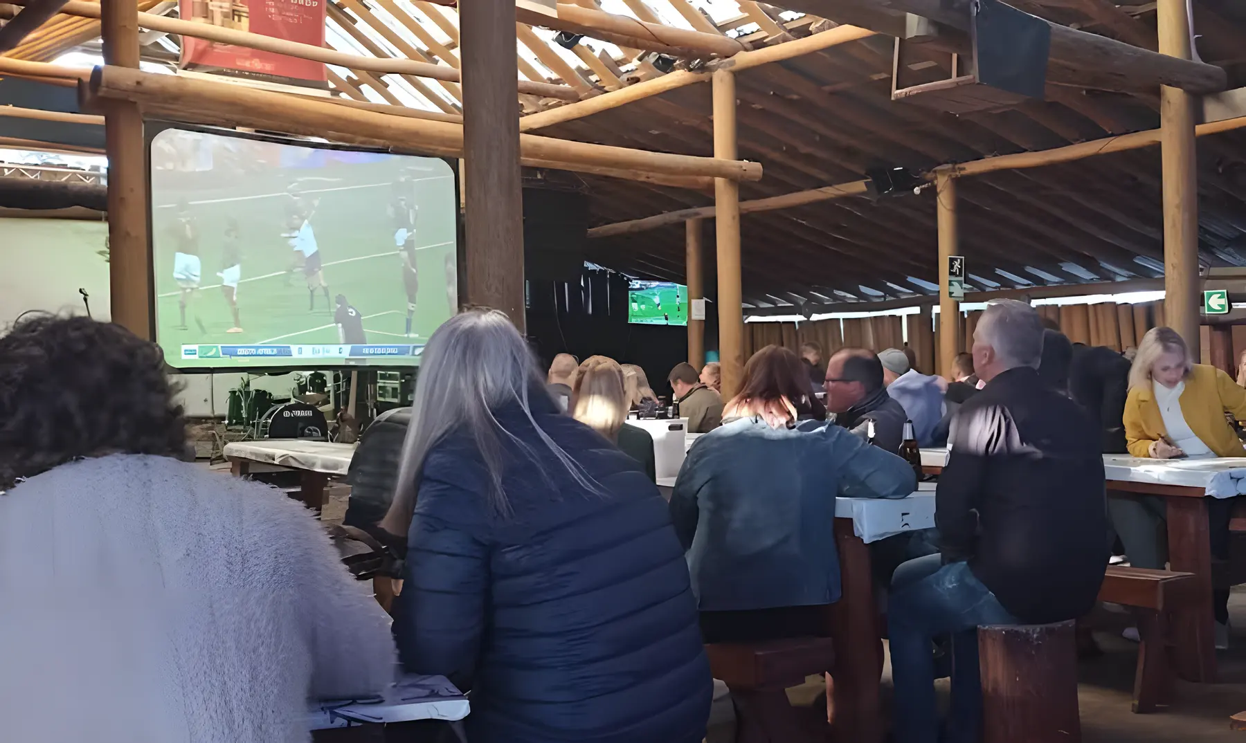 Guests at long tables in the lapa, watching rugby on a big screen
