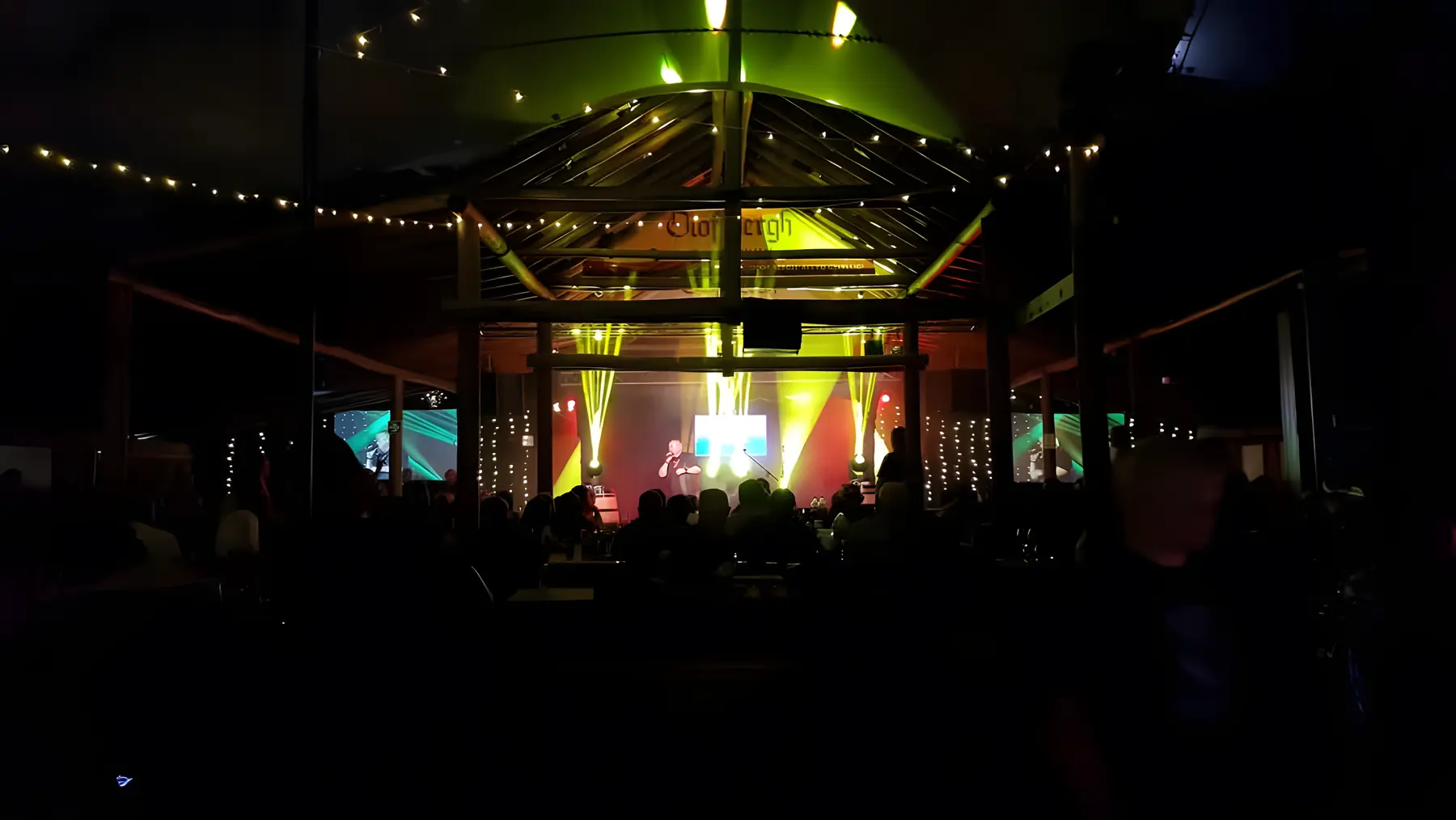 The lapa stage at night under green lights, with festoon lights strung along the roof